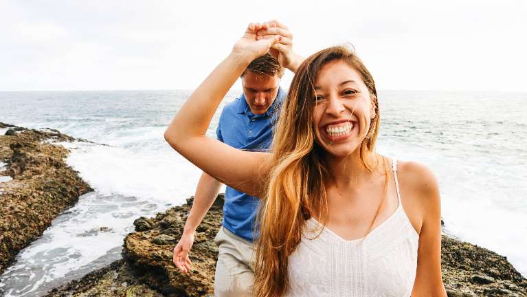 woman smiling and holding hands with male partner next to the ocean